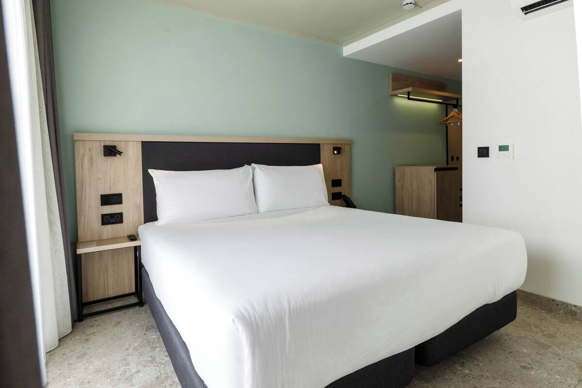 A neatly made bed in a hotel room with a wooden headboard, a nightstand, and a wardrobe.