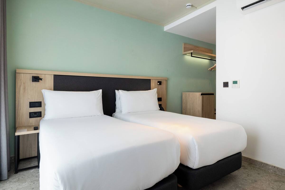 A twin room with two beds, a wooden headboard, bedside tables, and a built-in shelf.