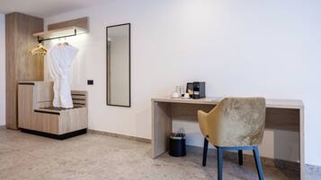 Una habitación de hotel moderna con un escritorio de madera, una silla, una bata colgada en un perchero, una cafetera y un cubo de basura.
