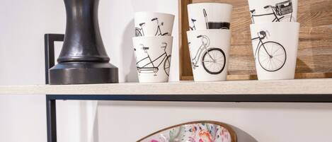 Una estantería con tres cuencos de madera que contienen frutas y pasteles, junto con tres tazas blancas decoradas con diseños de bicicleta.