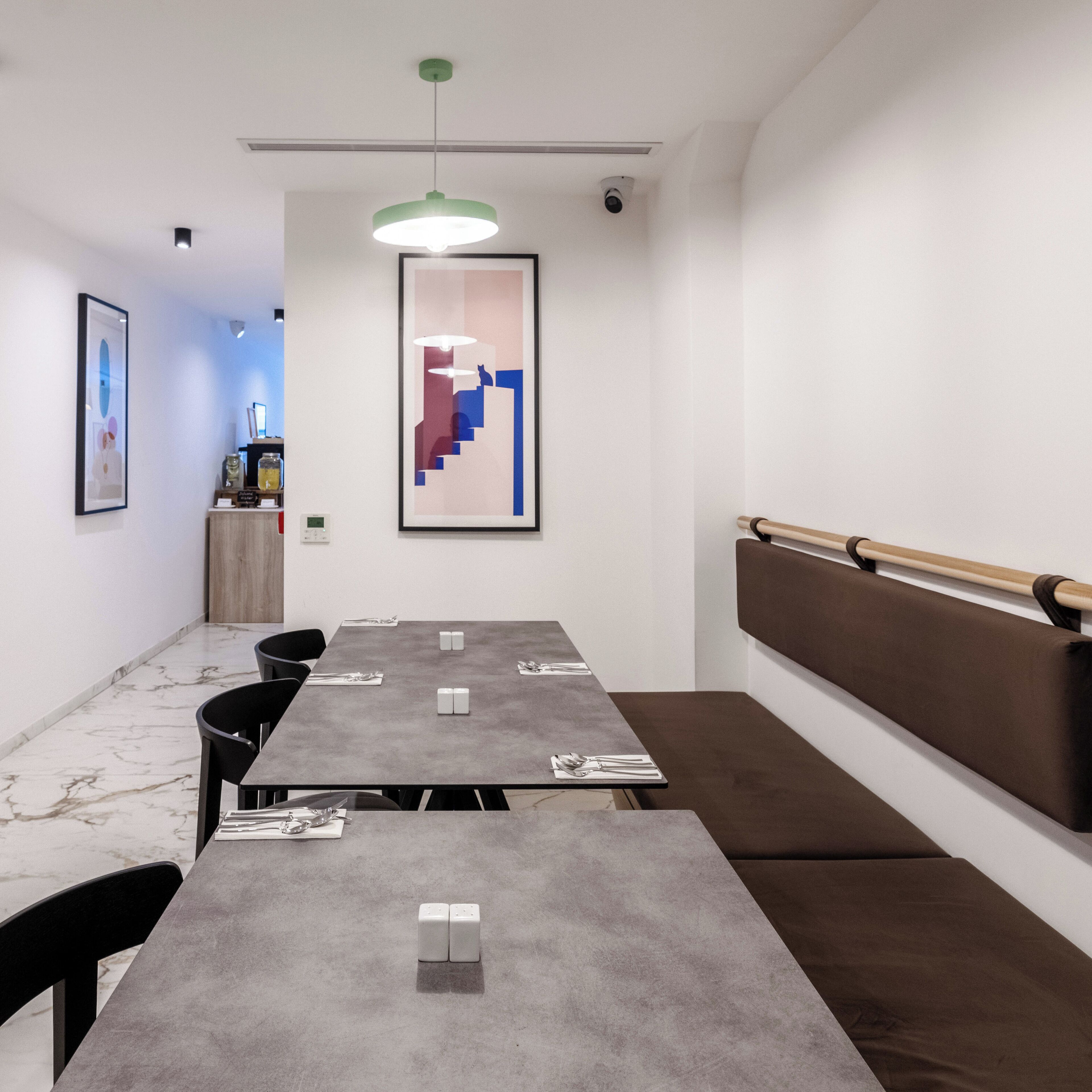Un salón de conferencias con una larga mesa, sillas, un banco, una lámpara colgante verde y una obra de arte abstracta enmarcada en la pared.