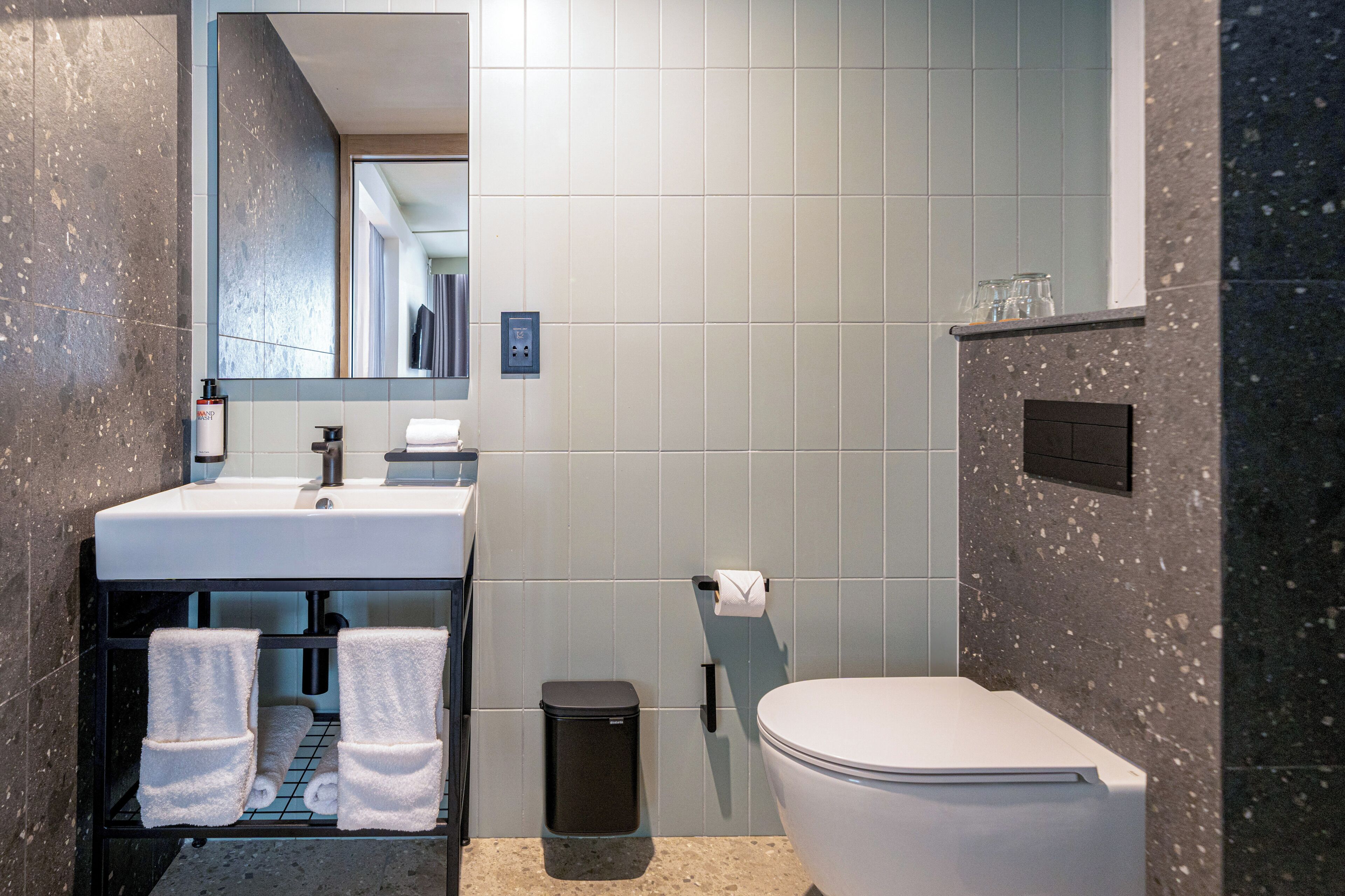 A modern bathroom with a white sink, black trash bin, and a toilet.