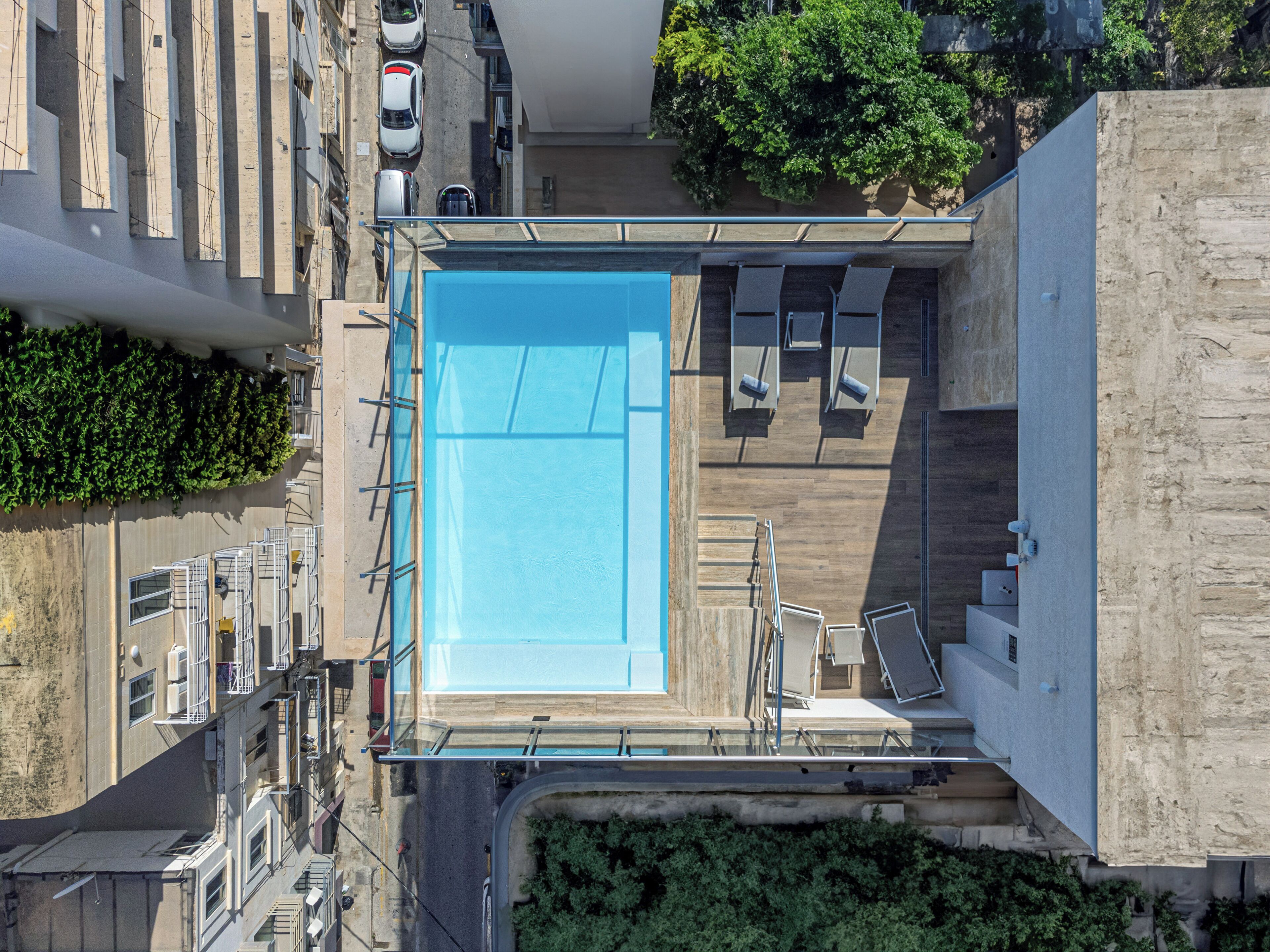 An aerial view of a rooftop pool with a clear blue pool, surrounded by a wooden deck and lounge chairs.