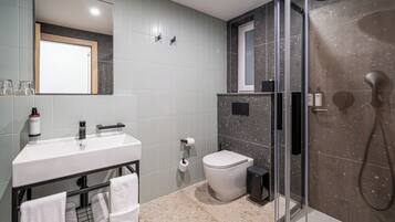 Un baño moderno con lavamanos blanco, inodoro, cabina de ducha con mampara de vidrio y espejo sobre el lavamanos.