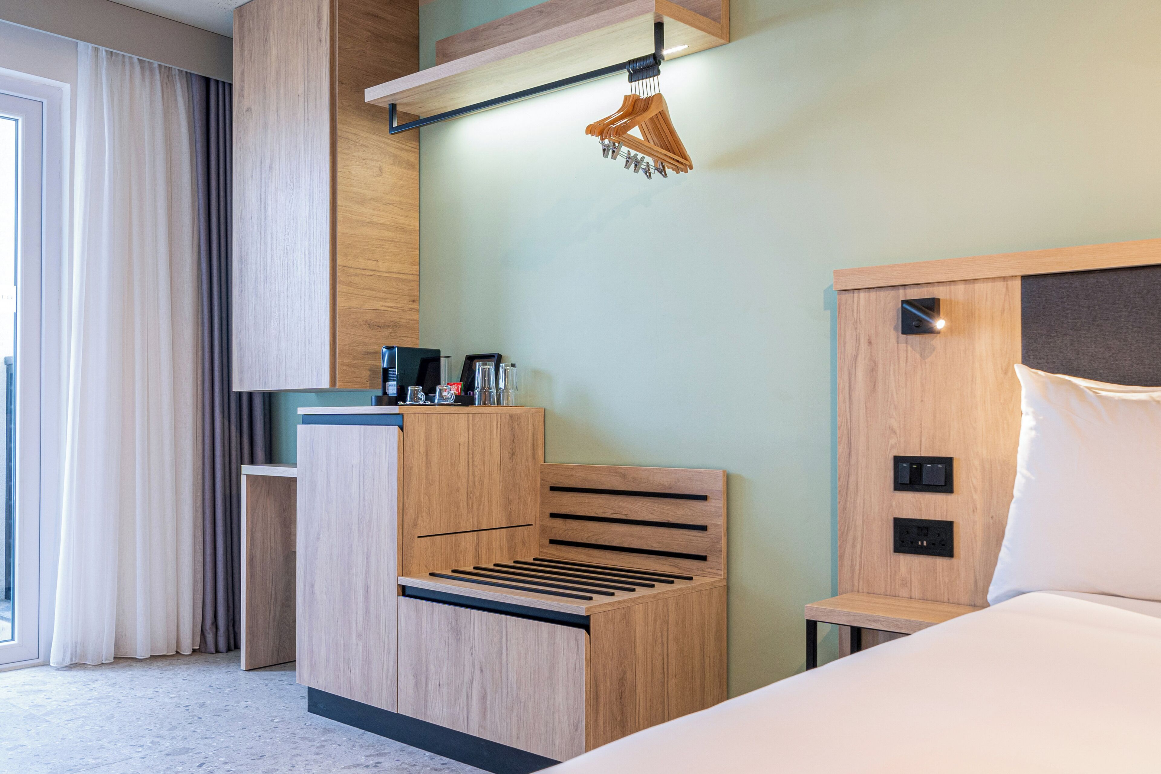 Una habitación de hotel moderna con una cama de madera, un escritorio pequeño y un perchero de madera colgante.
