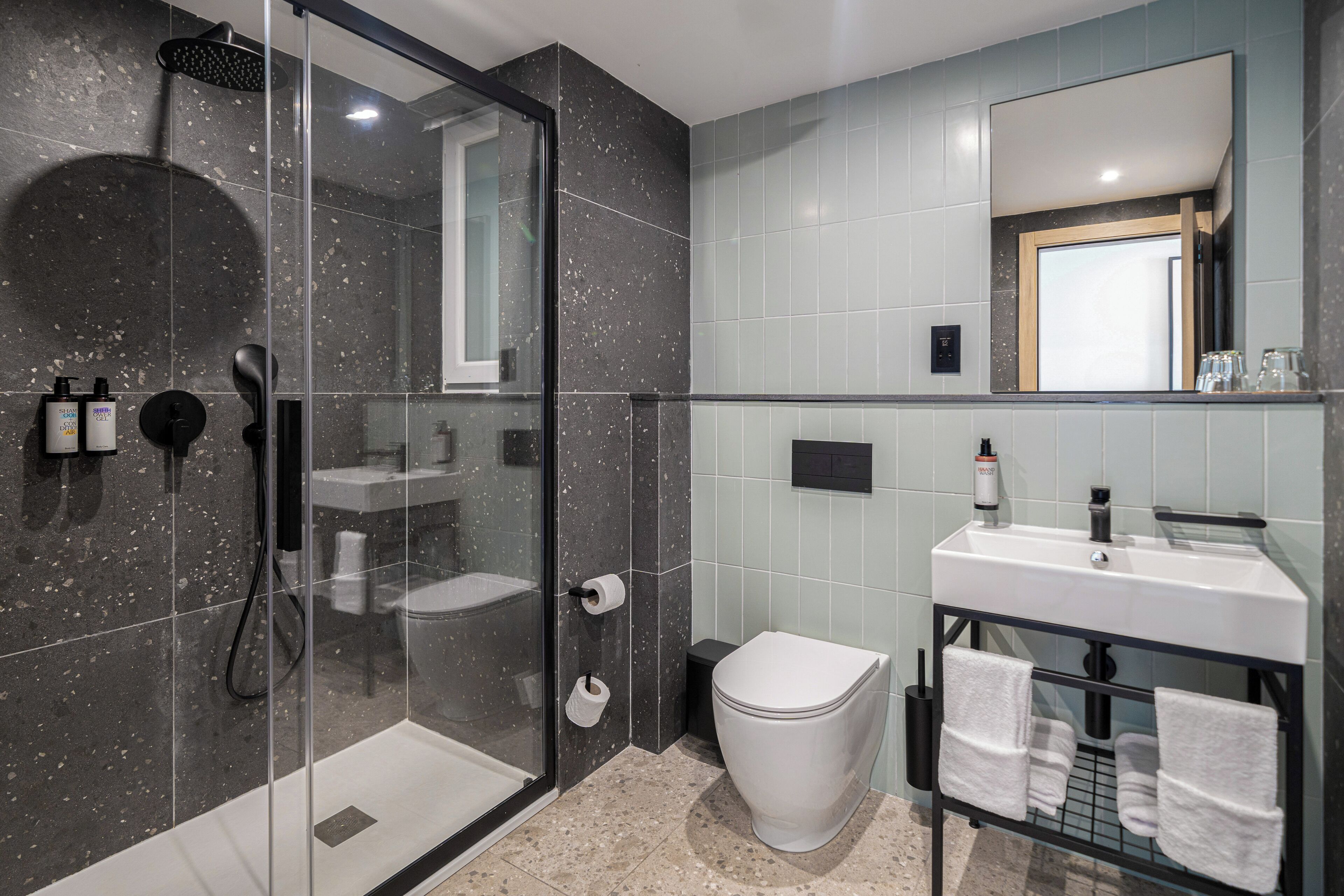 A modern bathroom with a glass-enclosed shower, a white toilet, and a vanity with a mirror and towel rack.