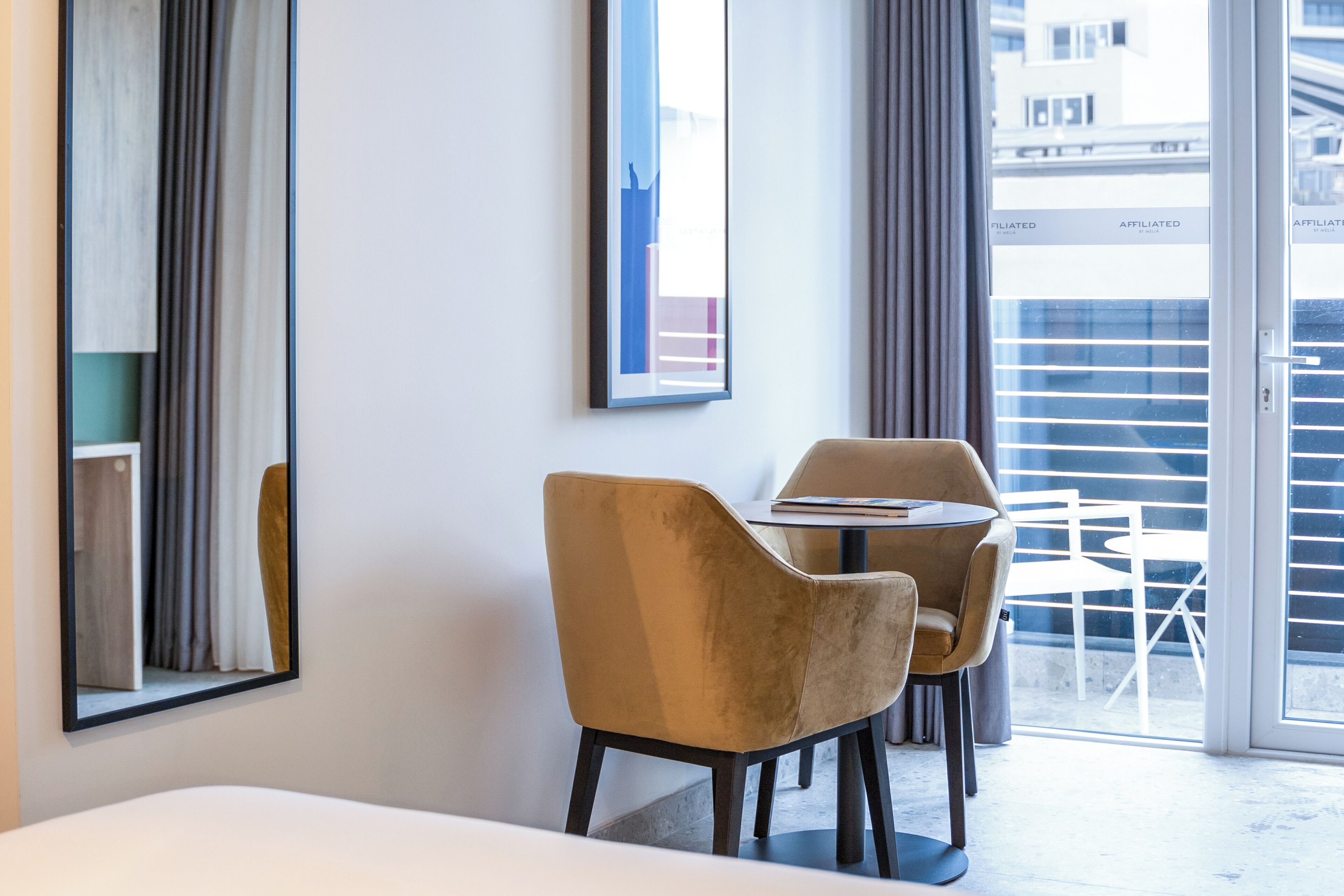 A modern hotel room with a large window, a bed, a small table, and two chairs.