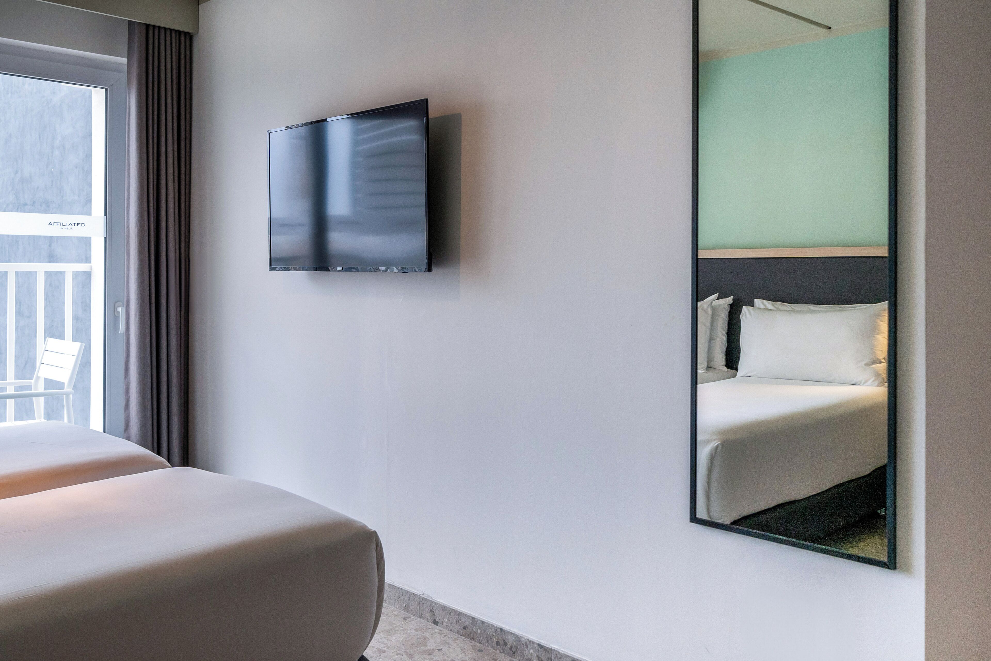 A hotel room with a bed, a television mounted on the wall, and a large mirror reflecting the bed.