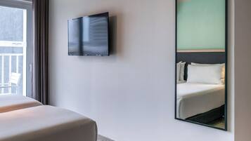 A hotel room with a bed, a television mounted on the wall, and a large mirror reflecting the bed.