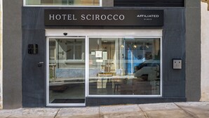 The exterior of Hotel Scirocco with a modern facade, large glass entrance, and a sign indicating affiliation with Melia.