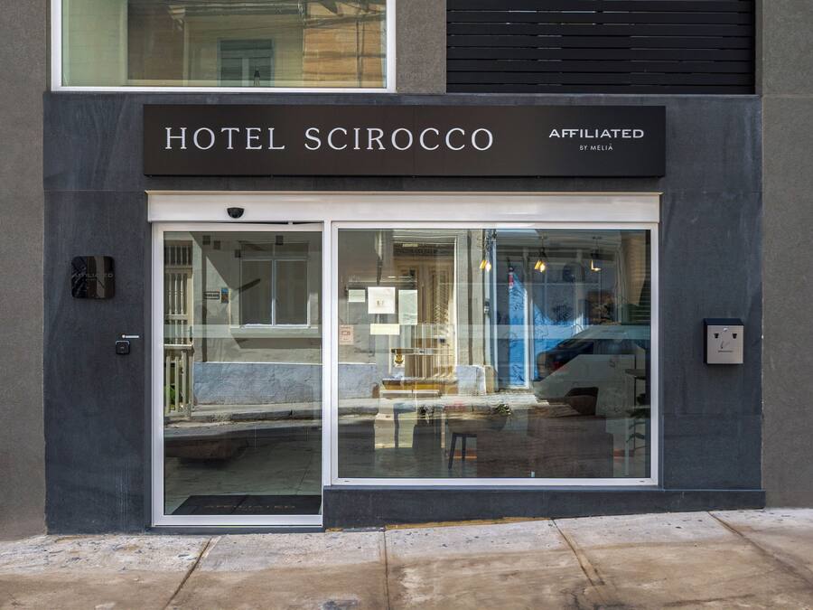 The exterior of Hotel Scirocco with a modern facade, large glass entrance, and a sign indicating affiliation with Melia.