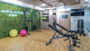 Un gimnasio con equipamiento de ejercicio, una pared verde con el texto 'AFFILIATED BY MELIA' y suelo de madera.