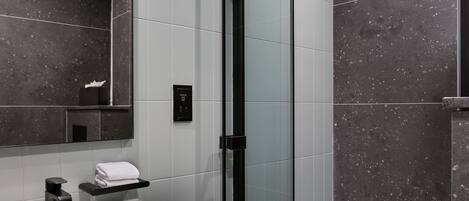 Un baño moderno con ducha envuelta en vidrio, un lavamanos blanco y un espejo grande.