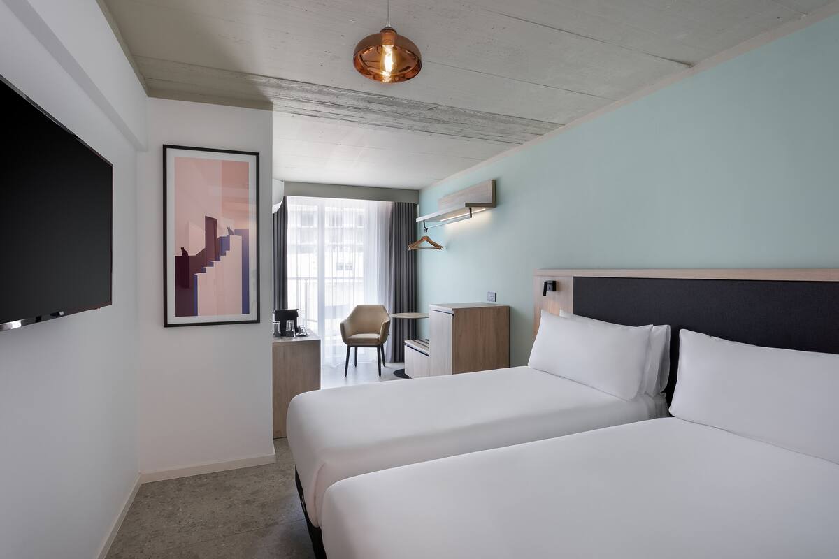 A hotel room with a large bed, a desk, a chair, and a TV mounted on the wall.