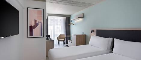 A hotel room with a large bed, a desk, a chair, and a TV mounted on the wall.