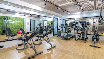 A modern gym with cardio machines, weight stations, and a green wall.