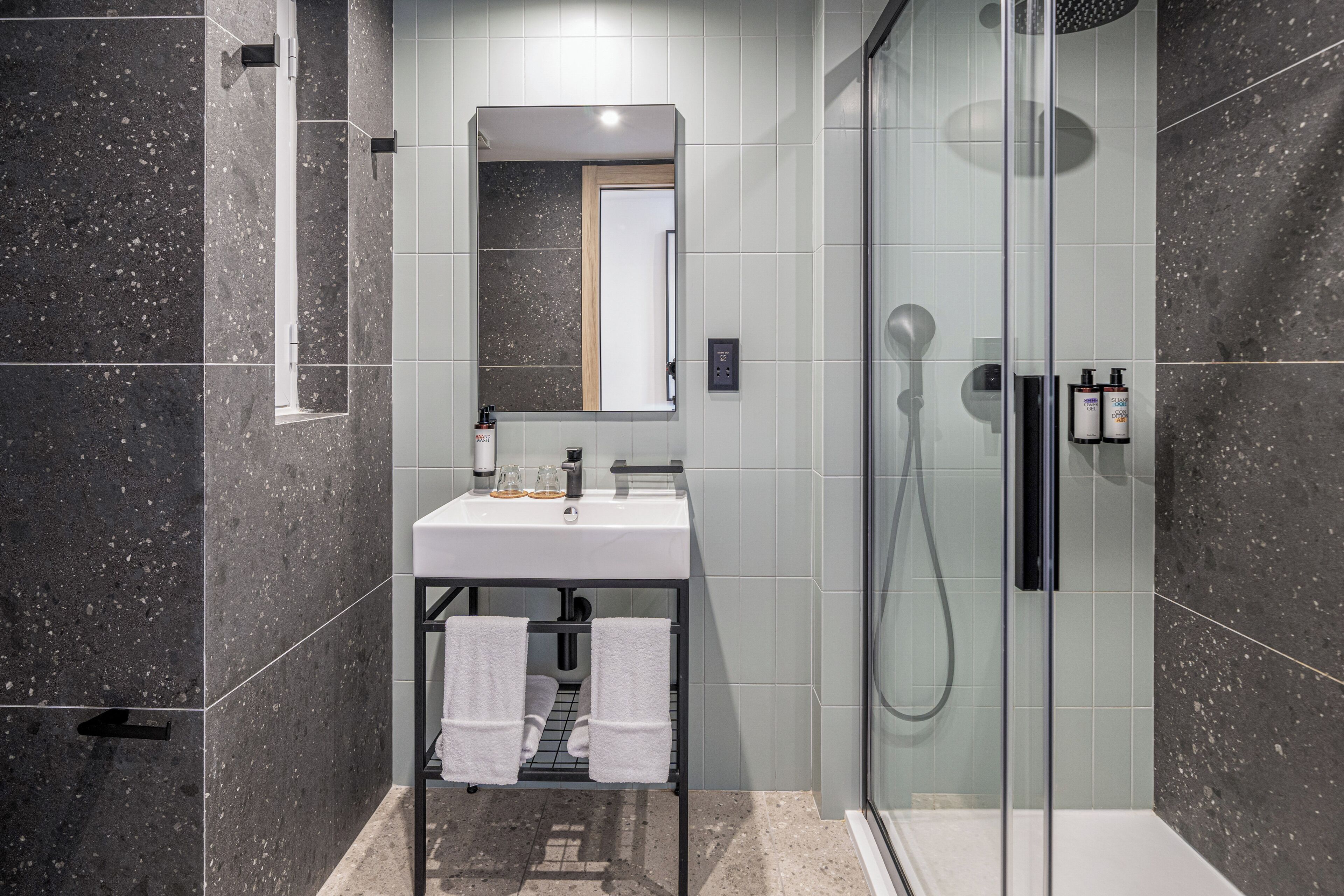 Et moderne badeværelse med en brusekabine i glas, en vask med toiletartikler og en bøjle til håndklæder.