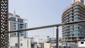 Un balcon avec une table et des chaises, donnant sur un paysage urbain composé d’immeubles modernes et de grues de construction.