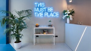 Un espace d'accueil moderne agrémenté d'un panneau lumineux au néon, d'une plante en pot et d'une petite table ornée d'objets décoratifs.