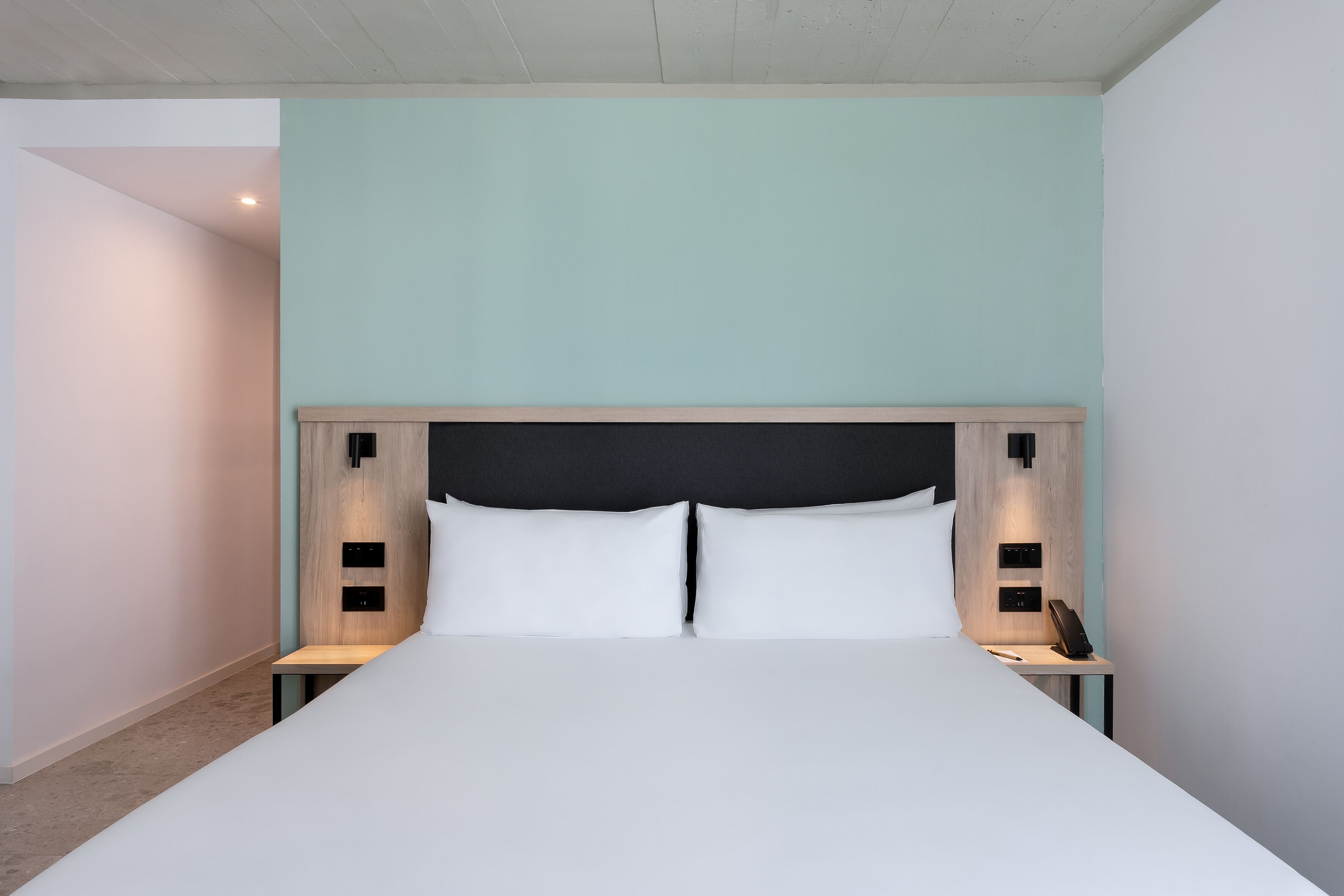 Una habitación de hotel moderna con una cama grande, cabecero de madera y mesitas de noche con lámparas.