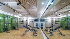 Une salle de sport avec des murs recouverts de miroirs, un plancher en bois et divers appareils d’exercice.