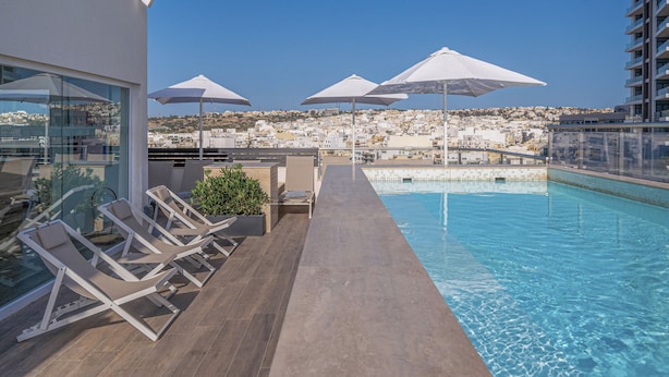 Un espace piscine aménagé sur le toit, avec des chaises longues et des parasols, offrant une vue sur le paysage urbain.