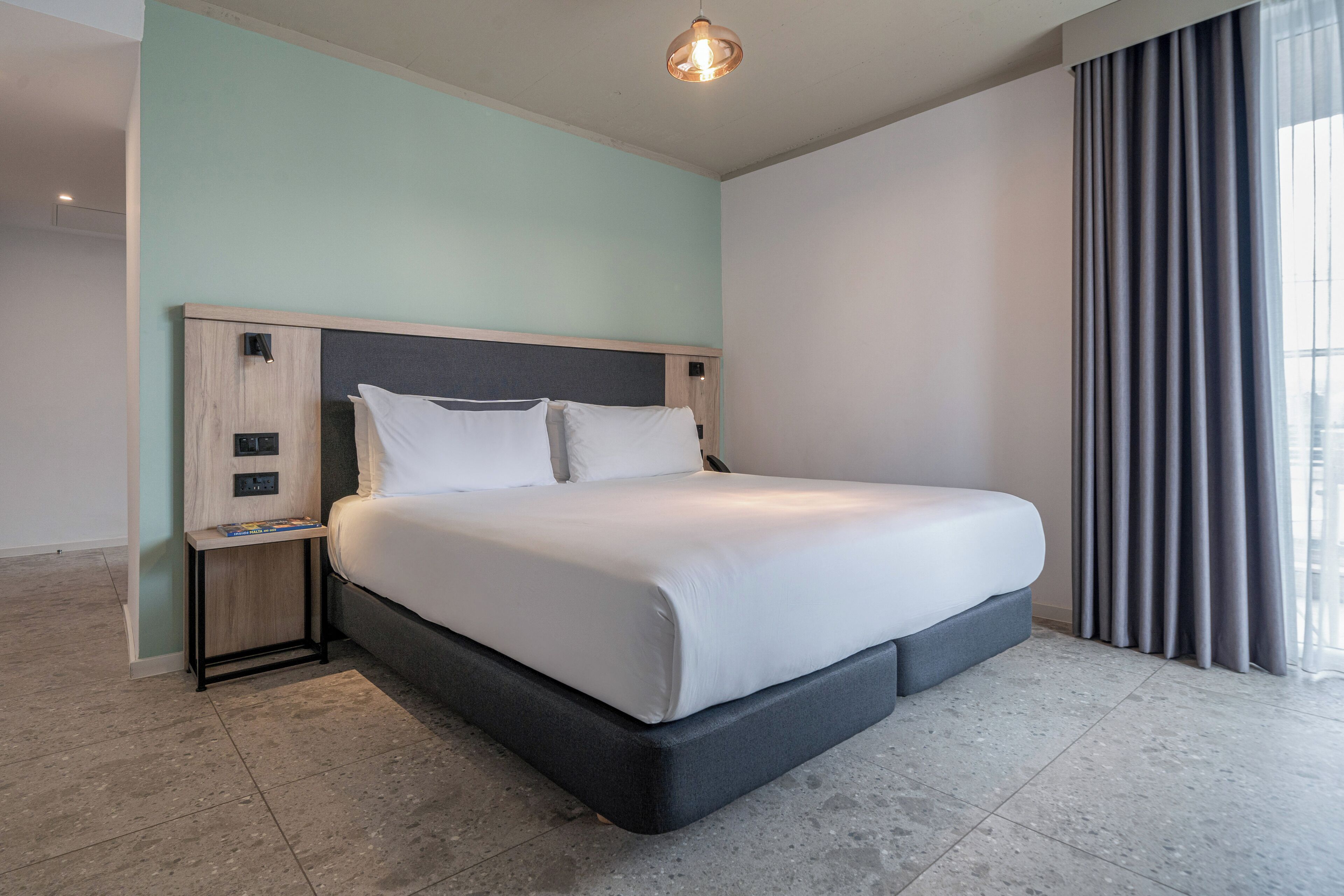 Ein modernes Hotelzimmer mit einem großen Bett, einem Nachttisch und einem Beistelltisch.
