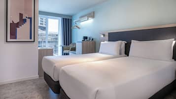 Habitación de hotel con dos camas, un escritorio, una silla y una ventana con cortinas.