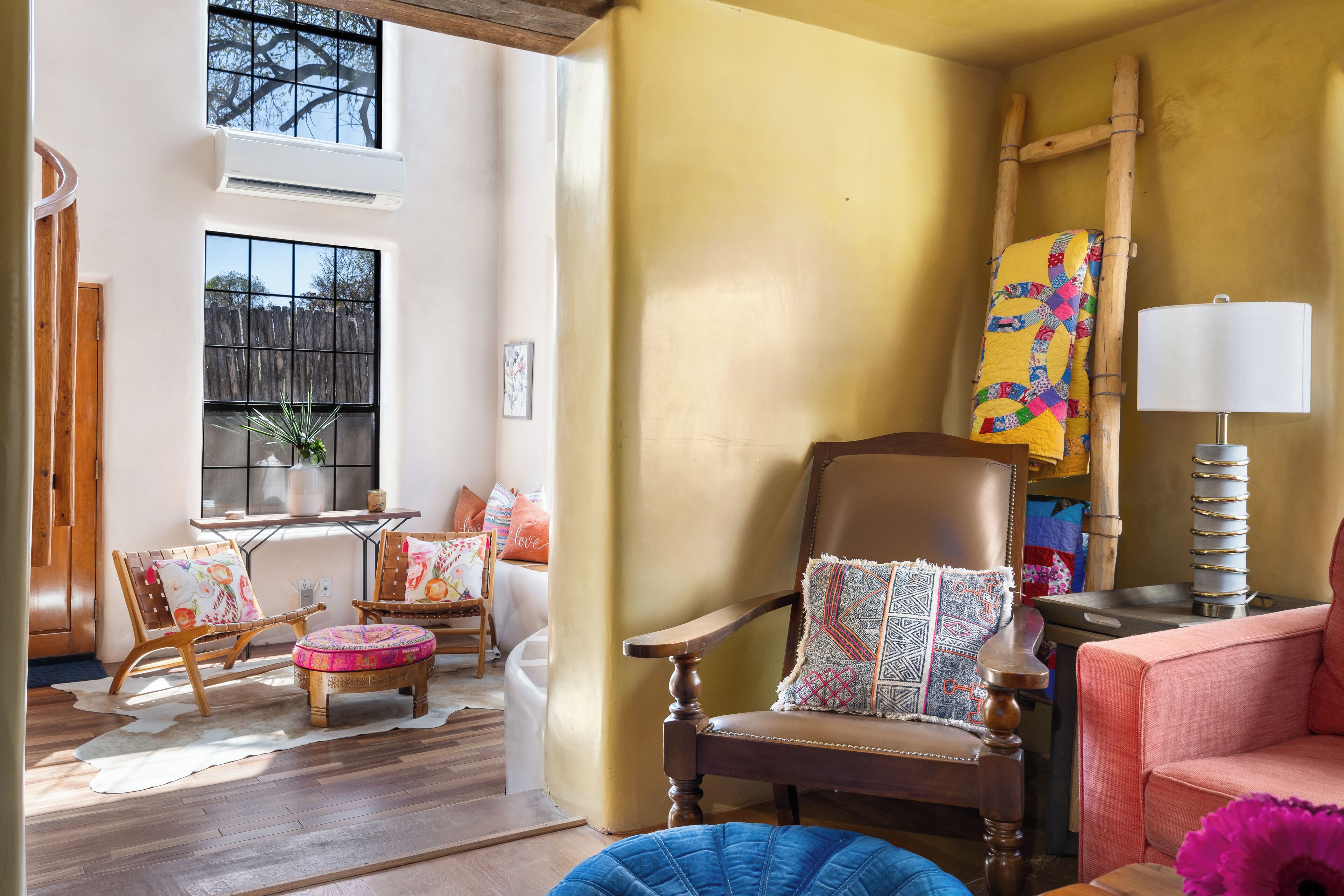 Een gezellige woonkamer met houten vloer, groot raam, open haard en een comfortabele zithoek met fauteuil en voetenbank.