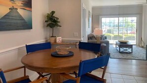 Comedor con una mesa redonda de madera, sillas azules, una planta en maceta y un cuadro de un muelle.