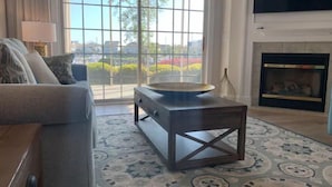 Una sala de estar con sofá, mesa de centro, chimenea y un ventanal con vistas a zonas verdes.