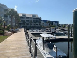 Uma marina com barcos atracados, um calçadão de madeira e um edifício de vários andares com sacadas.