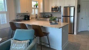 Una cocina moderna con armarios blancos, electrodomésticos de acero inoxidable y una isla central con taburetes de bar.