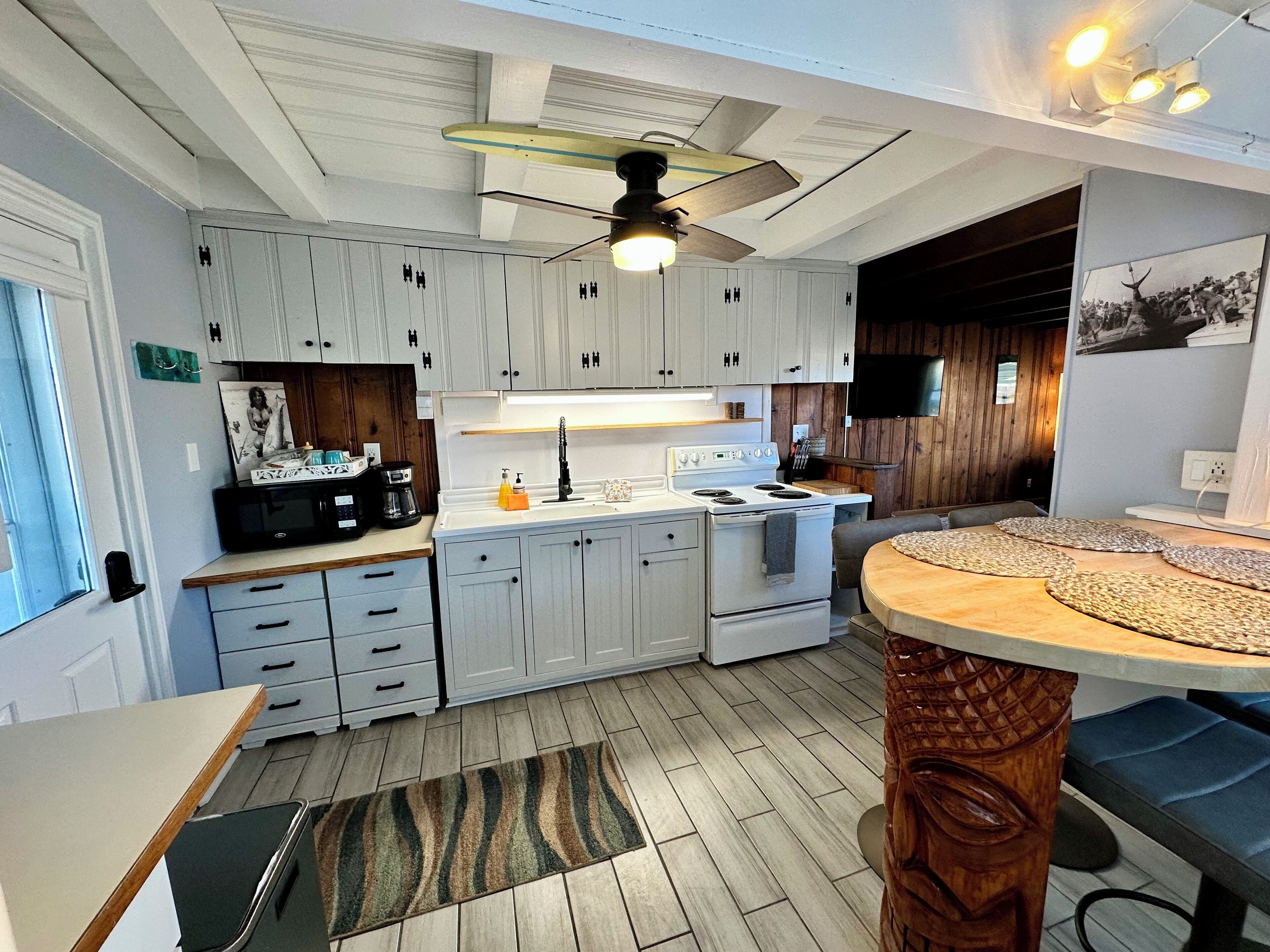 A compact kitchen with white cabinets, a stove, and a ceiling fan.