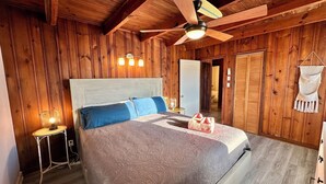A wooden-paneled room with a bed, a ceiling fan, and a nightstand with a lamp. - Sand Life - Pelican's Northern Nest -Pet Friendly! (Kill Devil Hills)