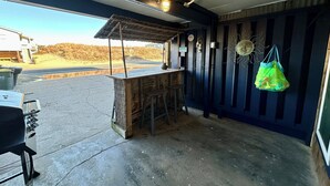 A food truck with a wooden counter and stools, a hanging bag, and a view of a road and landscape. - Sand Life - Pelican's Northern Nest -Pet Friendly! (Kill Devil Hills)