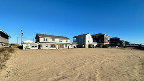 A residential area with multiple houses, a large open sandy area, and a clear blue sky. - Sand Life - Pelican's Northern Nest -Pet Friendly! (Kill Devil Hills)