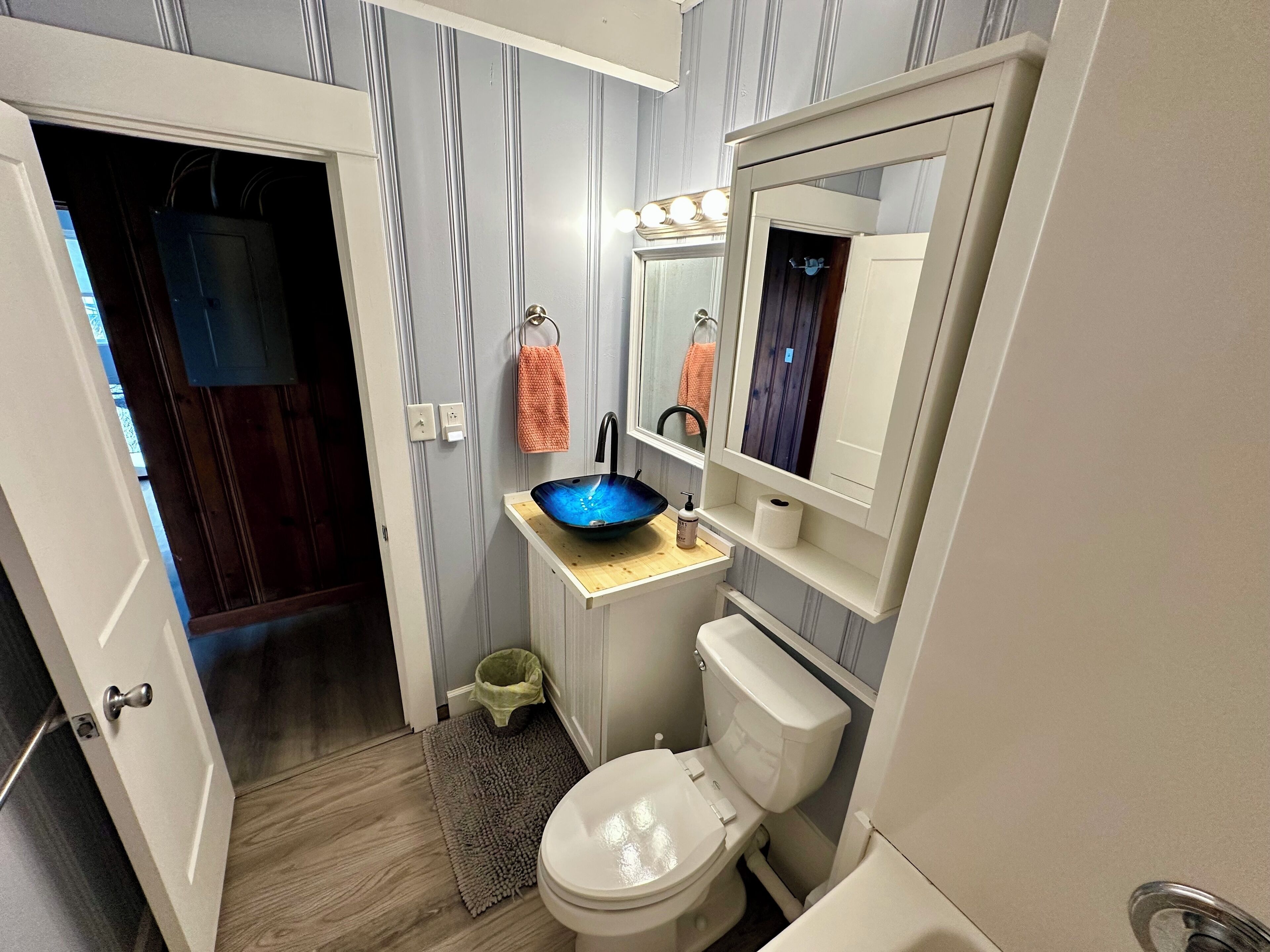 Une petite salle de bain avec des toilettes blanches, un lavabo bleu et un miroir au-dessus.