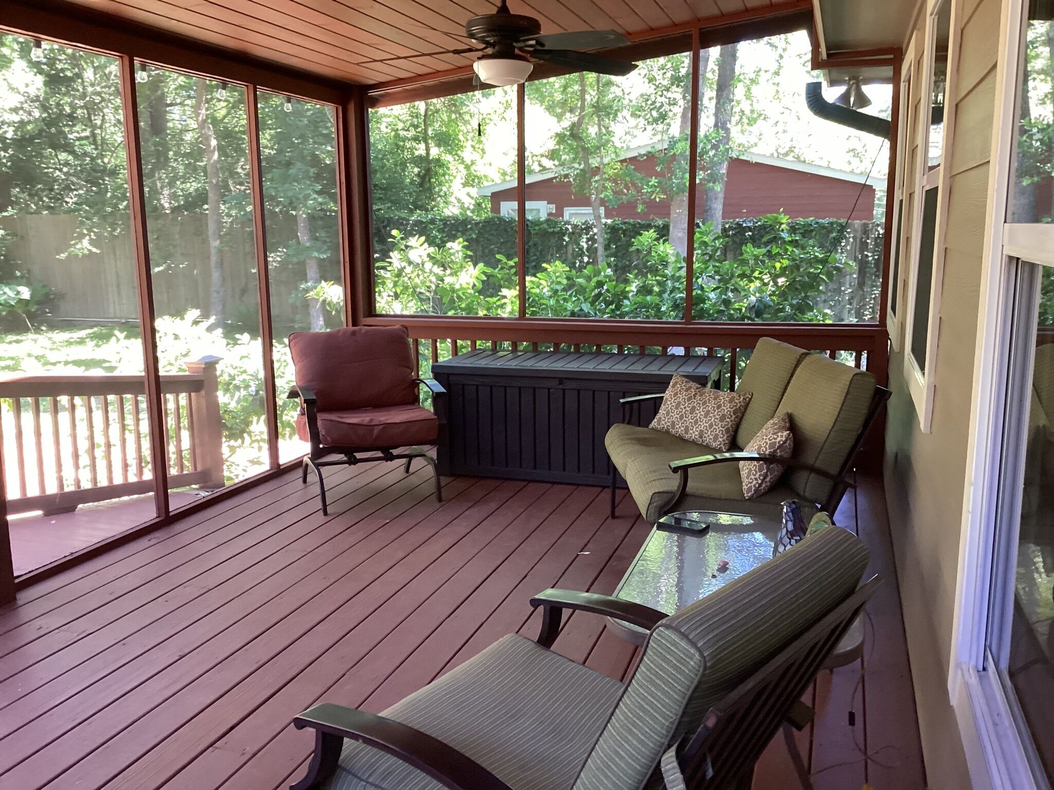 A covered outdoor deck with wooden flooring, a glass door, and a seating area with chairs and a table.