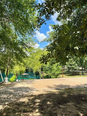 A sandy volleyball court surrounded by trees and a clear blue sky. - The Manor_4 BR w/ Pool Table, Swimming Pond, and Sand Volleyball (Montgomery)