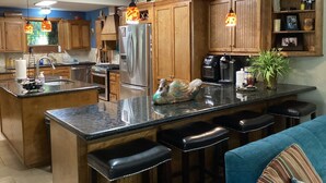 Una cocina moderna con armarios de madera, un refrigerador de acero inoxidable, una isla grande con taburetes de bar e iluminación colgante.
