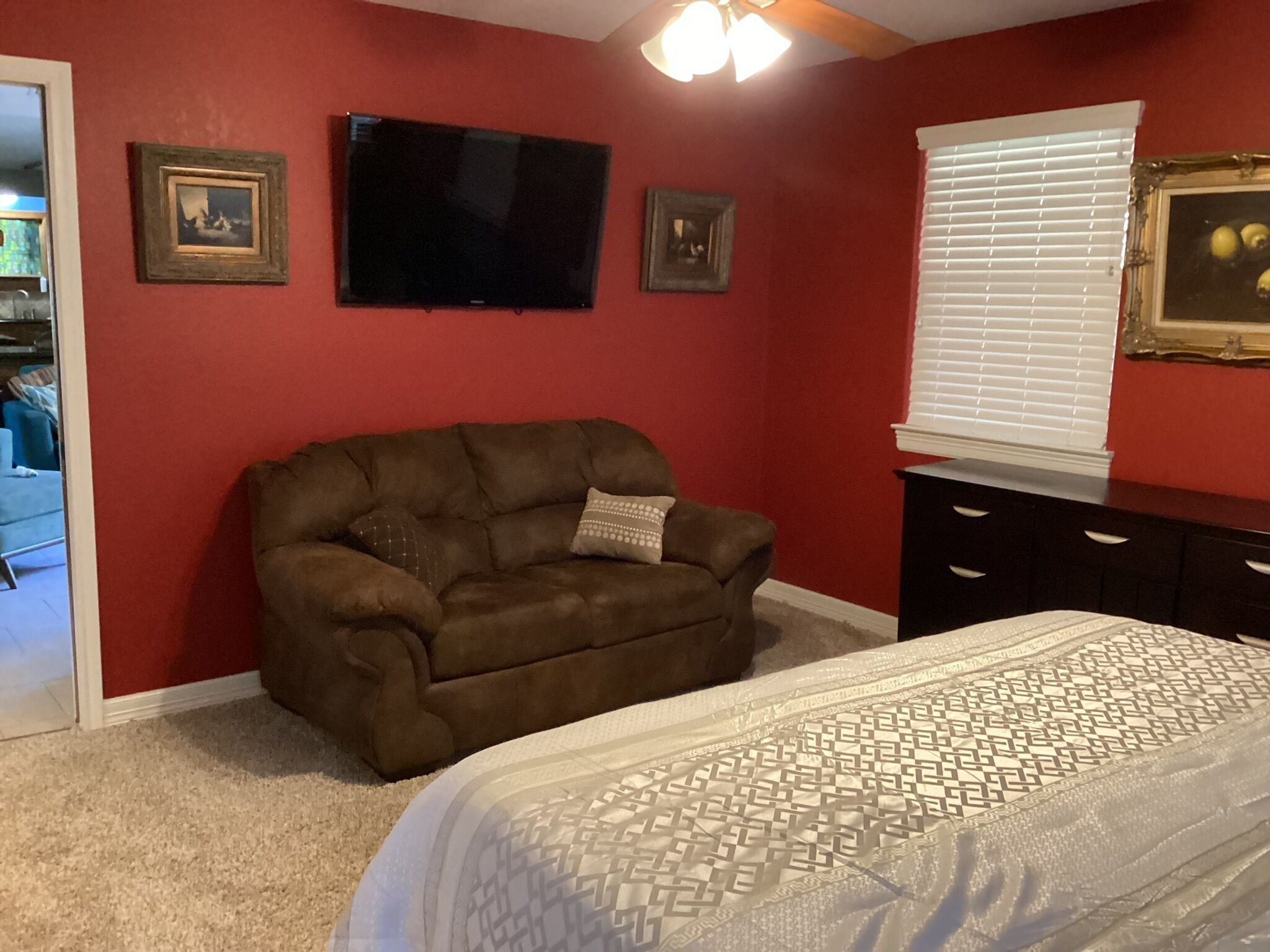 A bedroom with a brown leather chair, a bed with patterned bedding, a TV on the wall, and a window with blinds.