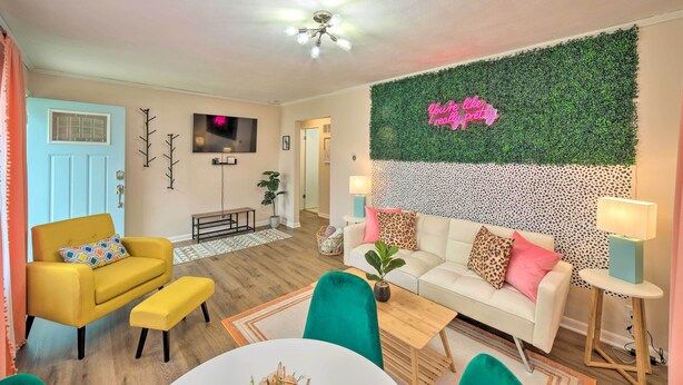 A living room with a yellow armchair, a white sofa, a green chair, and a small table. There is a neon sign on the wall and a ceiling fan. - *New* < 3 Miles to Beach + Casino + Zoo + Shopping! (Michigan City)