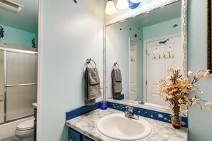 Un baño con lavamanos blanco, un espejo grande y un florero con flores.
