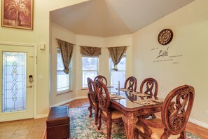 Un comedor con una mesa y sillas de madera, un tapete decorativo y una pared con un reloj y una cita.