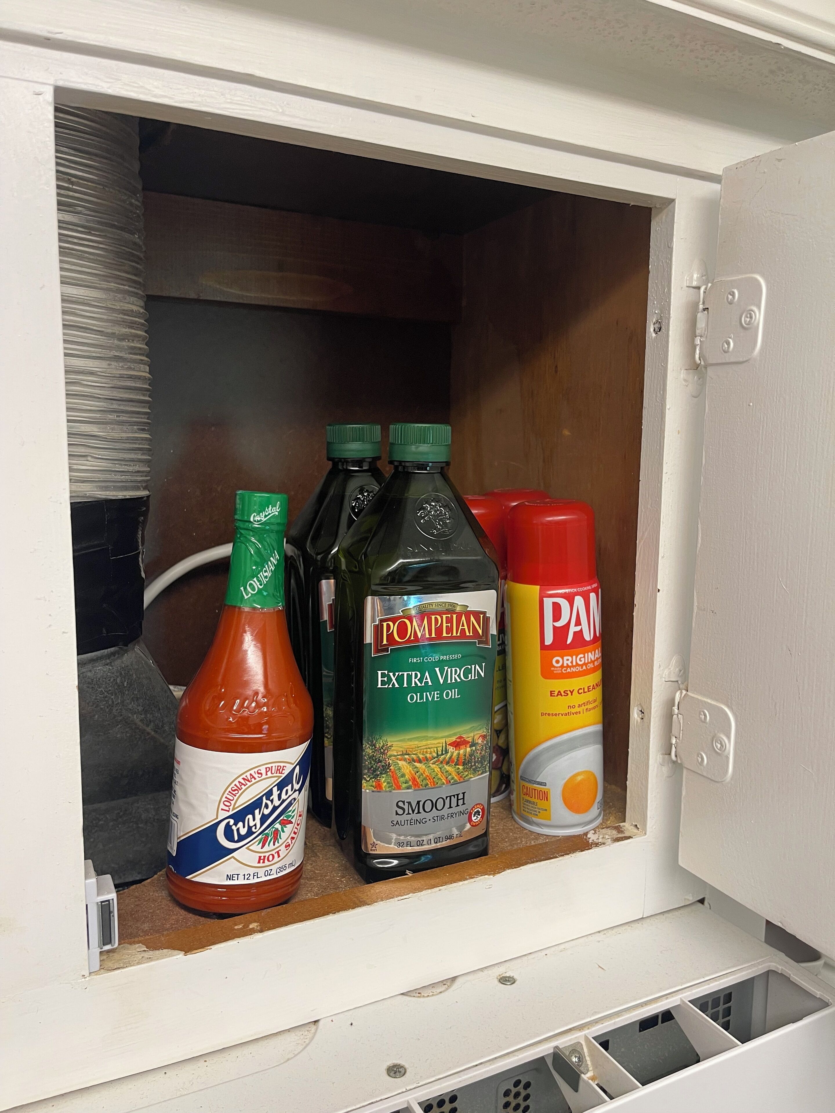 A cabinet containing various condiments including Crystal Hot Sauce, Pompeian Extra Virgin Olive Oil, and Pam Original Canola Oil.
