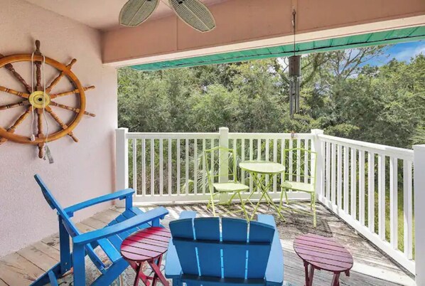 A covered outdoor seating area with a white railing, blue and red chairs, and a green table.