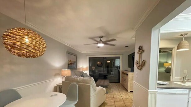A modern living room with a dining area, a ceiling fan, and a kitchen visible through an open door. - Redesigned condo in oceanfront community! (St. Simons Island)
