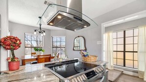 Une cuisine moderne dotée d’une cuisinière en acier inoxydable, d’une hotte en verre et d’un plan de travail en marbre.