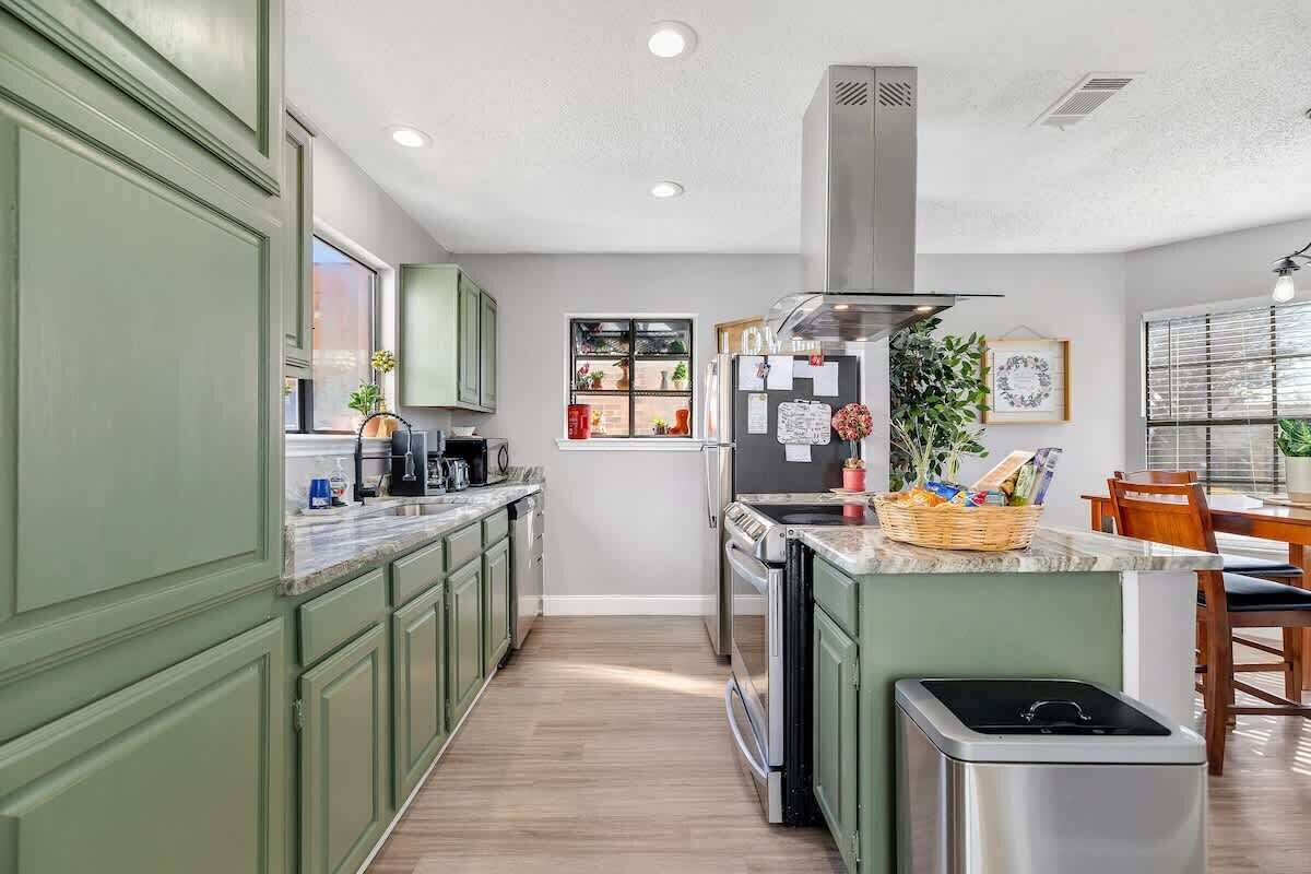 A kitchen with green cabinets, a stainless steel refrigerator, a built-in oven, and a dishwasher.